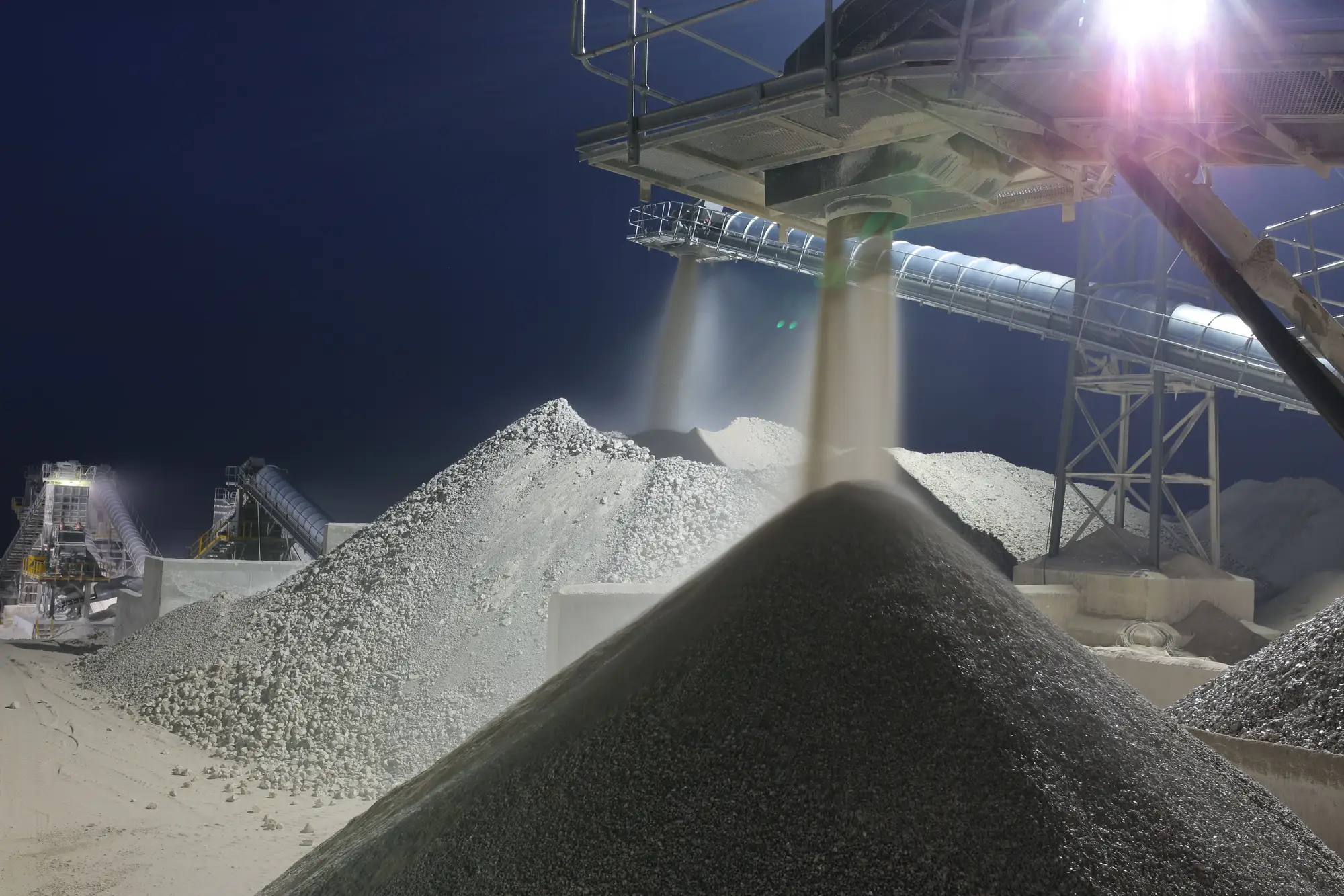 Sand and gravel stockpiles under conveyor lights at a processing plant at night